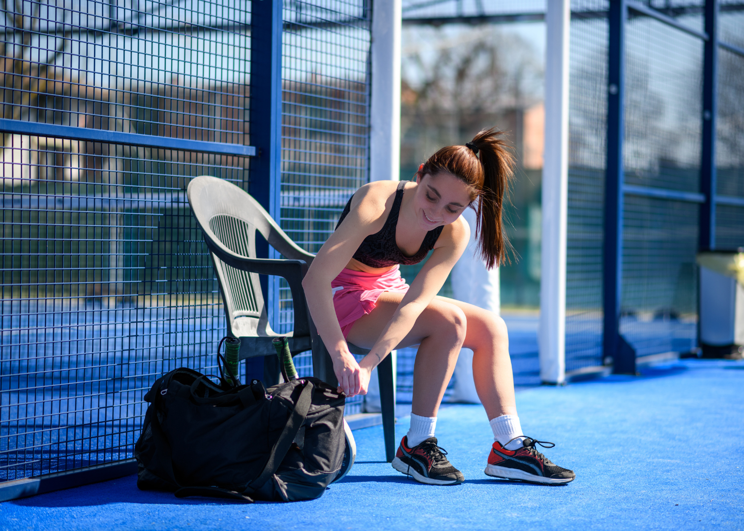 Woman tying her shoes on a blue sports court with a bag nearby.