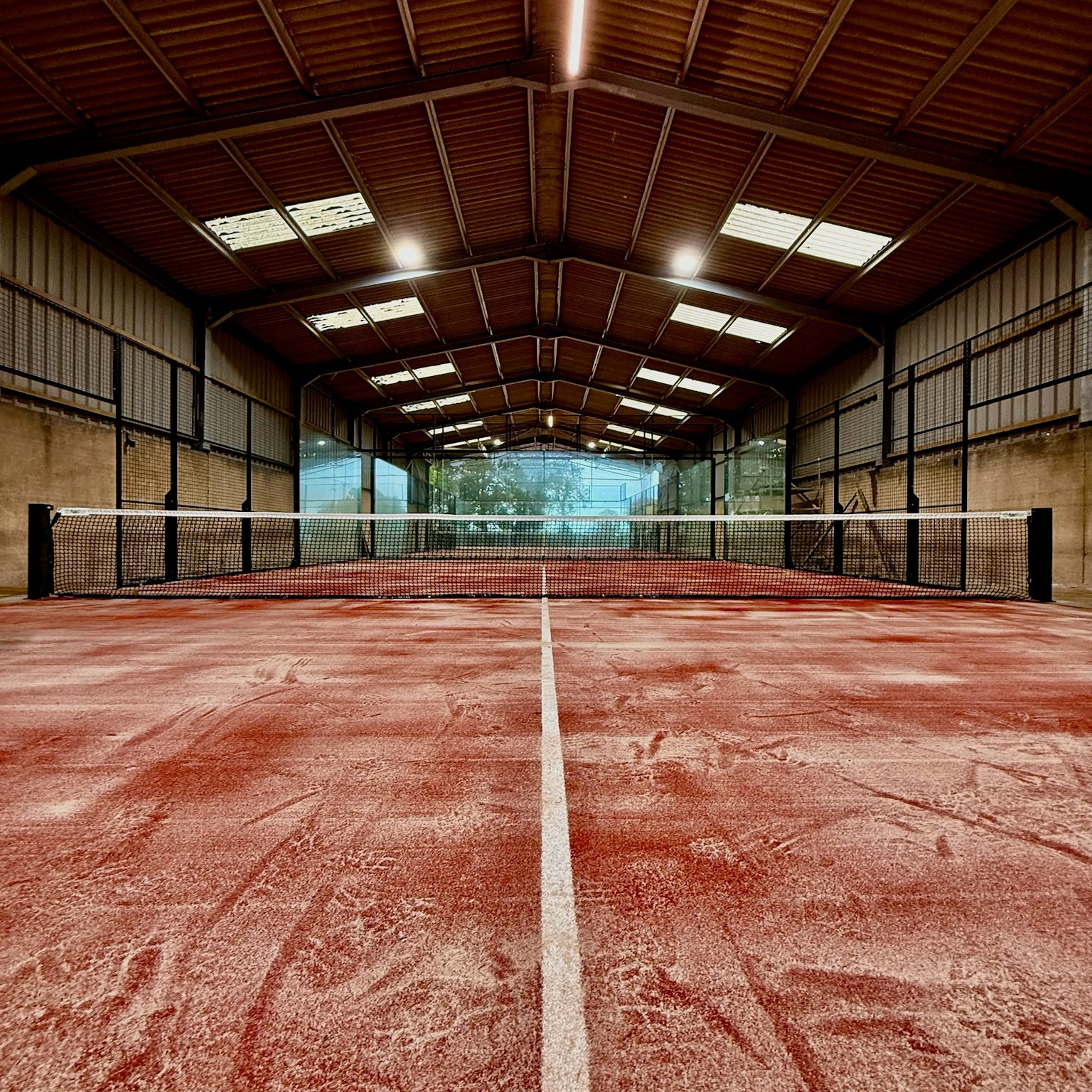 Indoor padel court inside a barn with a terraccotta coloured surface