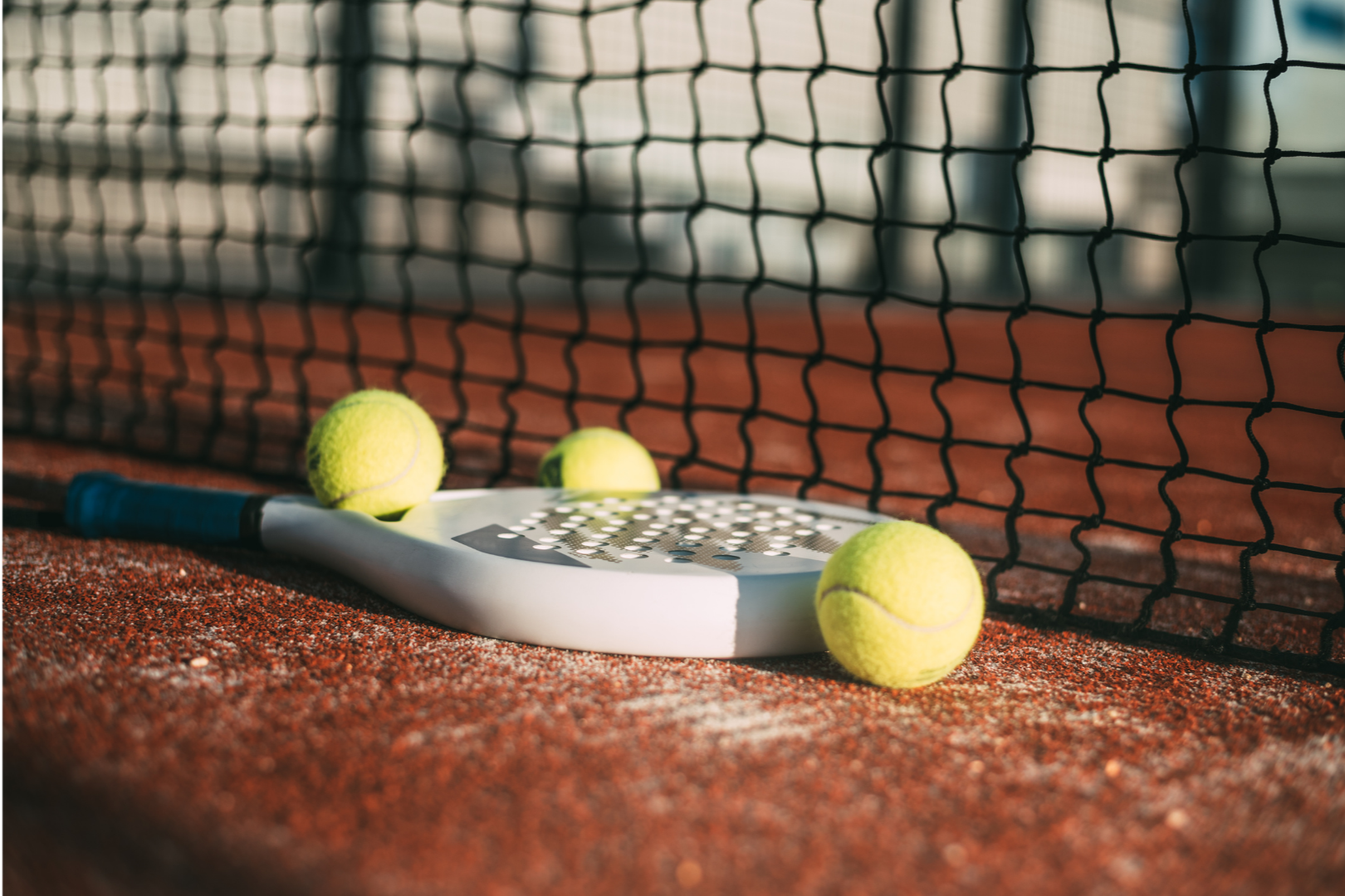 Padel tennis racket and balls on a clay court with net in the background