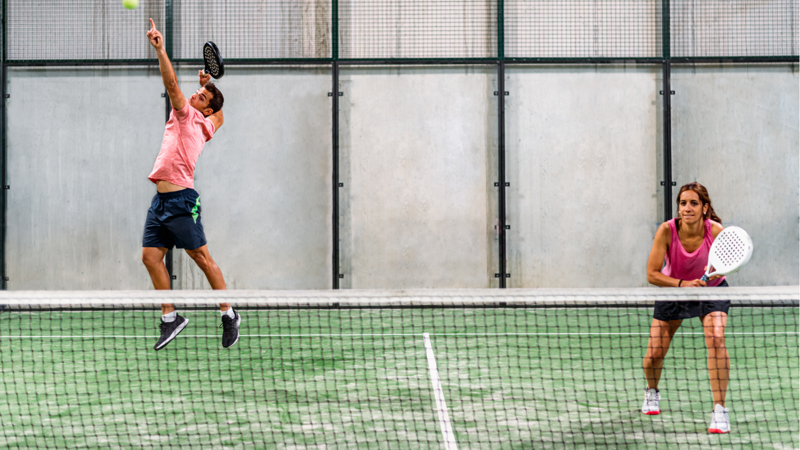 A man and woman playing padel tennis on a court with a net in the foreground.