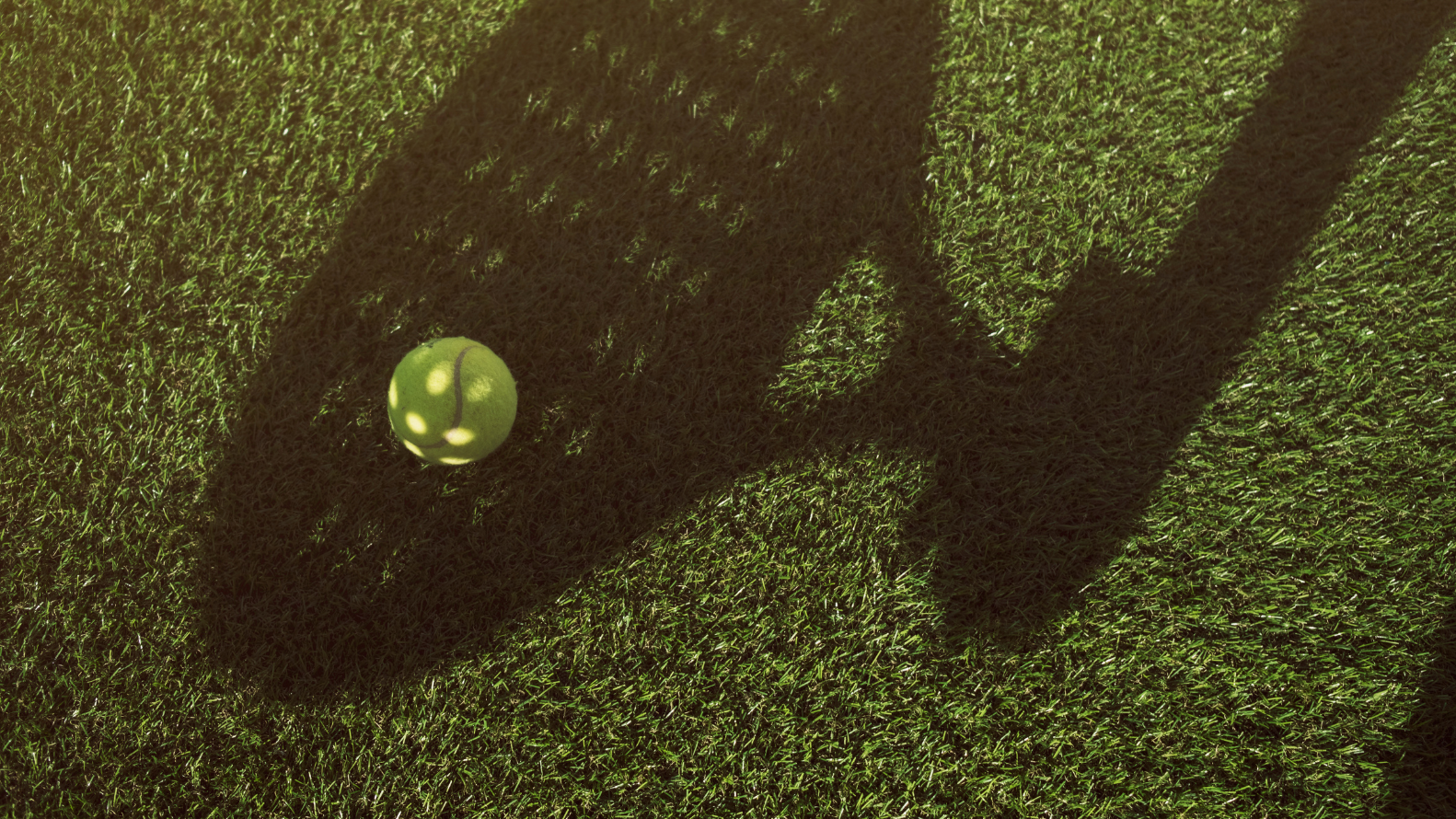 Shadow of a padel racket over a padel ball on a green turf surface