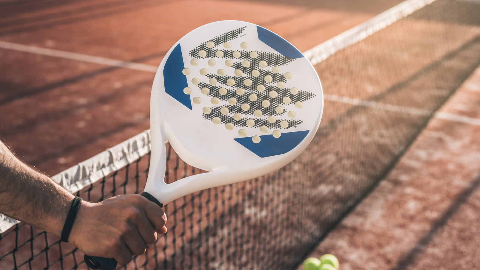 Padel racket with a held in front of the net over a padel court